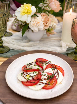 Caprese salad on a white plate with a decorative table setting including flowers and candles.