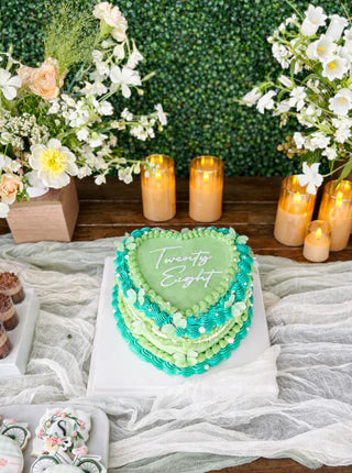 Heart-shaped cake with 'Twenty Eight' on a table with flowers and candles