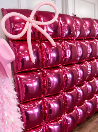 Pink inflatable balloons shaped like a bow on a decorative wall.
