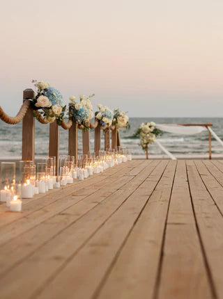 Decorative setup on a wooden pier with flowers and candles, overlooking the ocean.