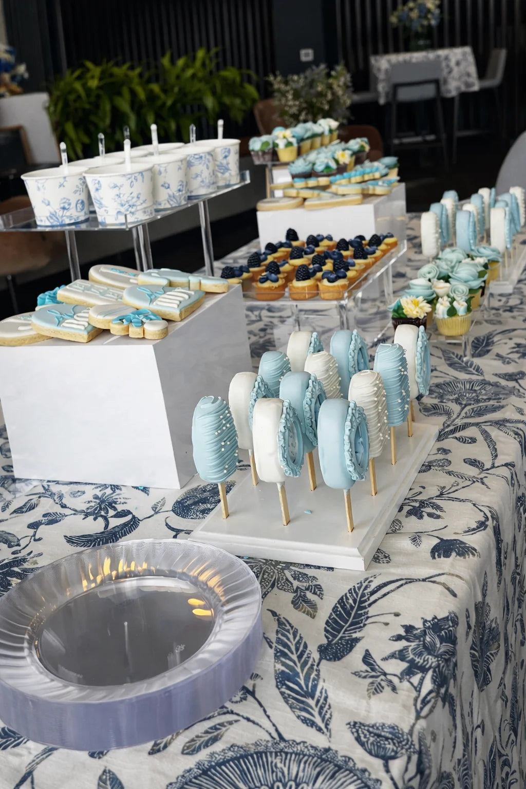 Decorative dessert table with cookies and cake pops on a patterned tablecloth.
